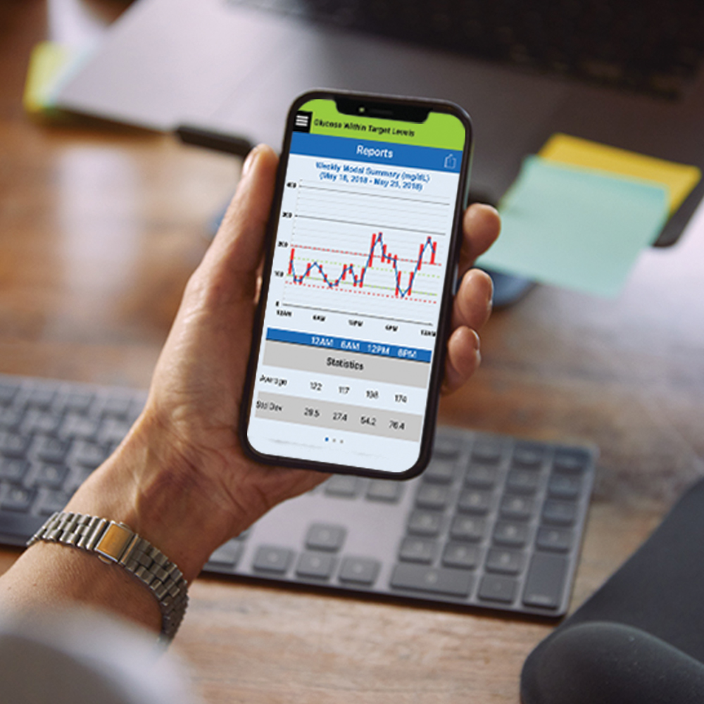 Woman sitting at her desk checks her glucose levels on the Eversense CGM app. 