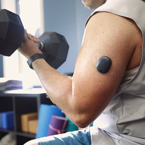 Man lifting weights while wearing a longterm CGM for diabetes. 