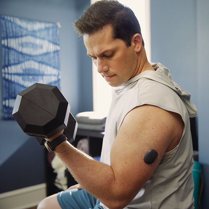 Man lifting weights at the gym while using a CGM system on his arm. 