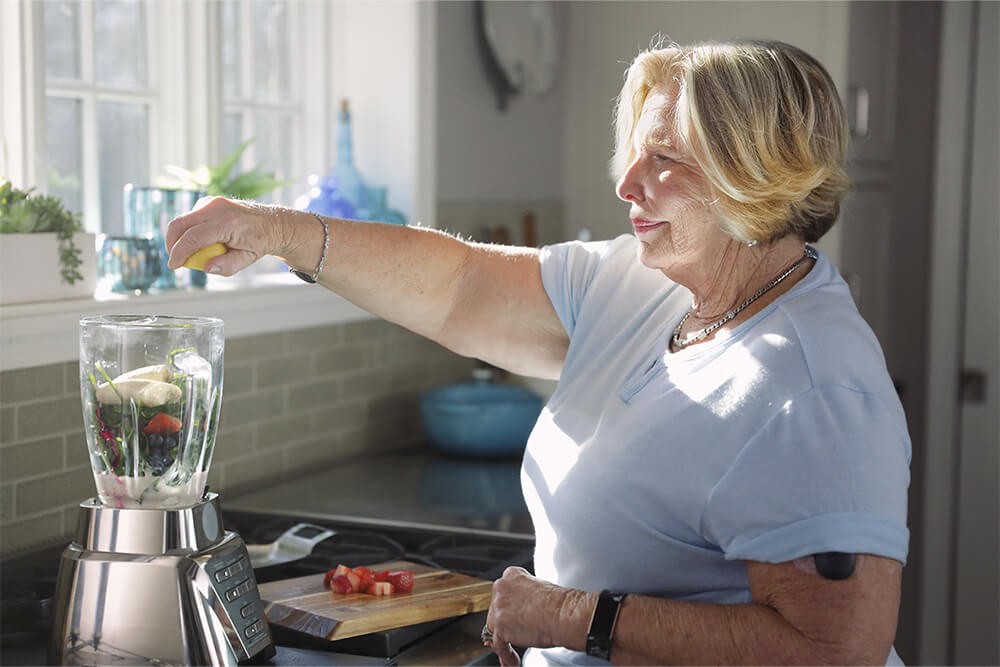 Woman blending a smoothie while using a continuous glucose monitoring device. 