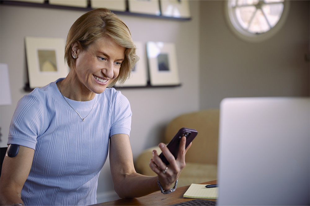 Woman using her phone to research coverage for an implantable CGM. 